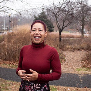 Professor April Copes, wearing a red turtleneck and standing outside on campus