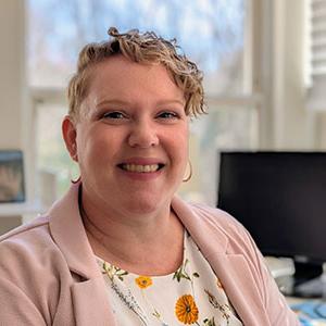 Headshot of KT Perkins with computer and window behind them